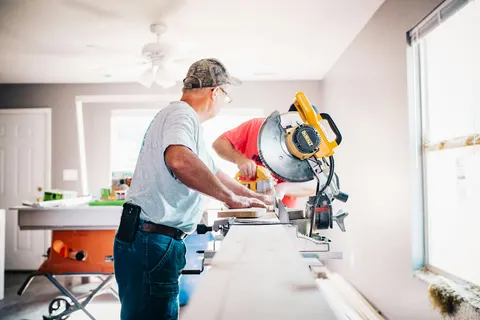 Two tradesmen cutting trim on a miter saw inside a house
