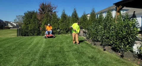 A two-person lawn crew mowing and trimming a large lawn