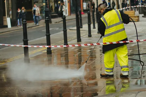 A worker in high-visibility gear pressure washing pavement